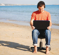 A man using a laptop with headphones on a beach