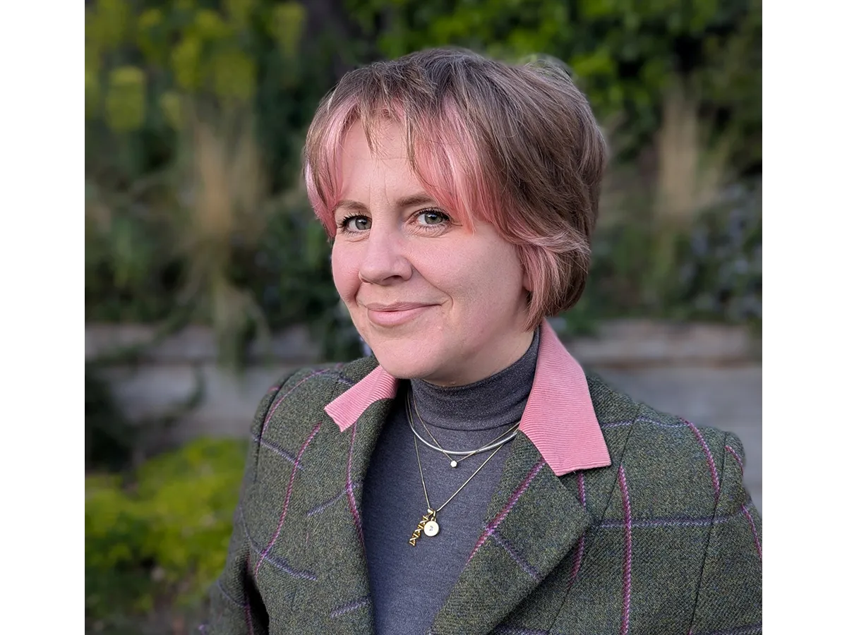 Headshot of Zoe smiling with pink hair and suit jacket and polarneck