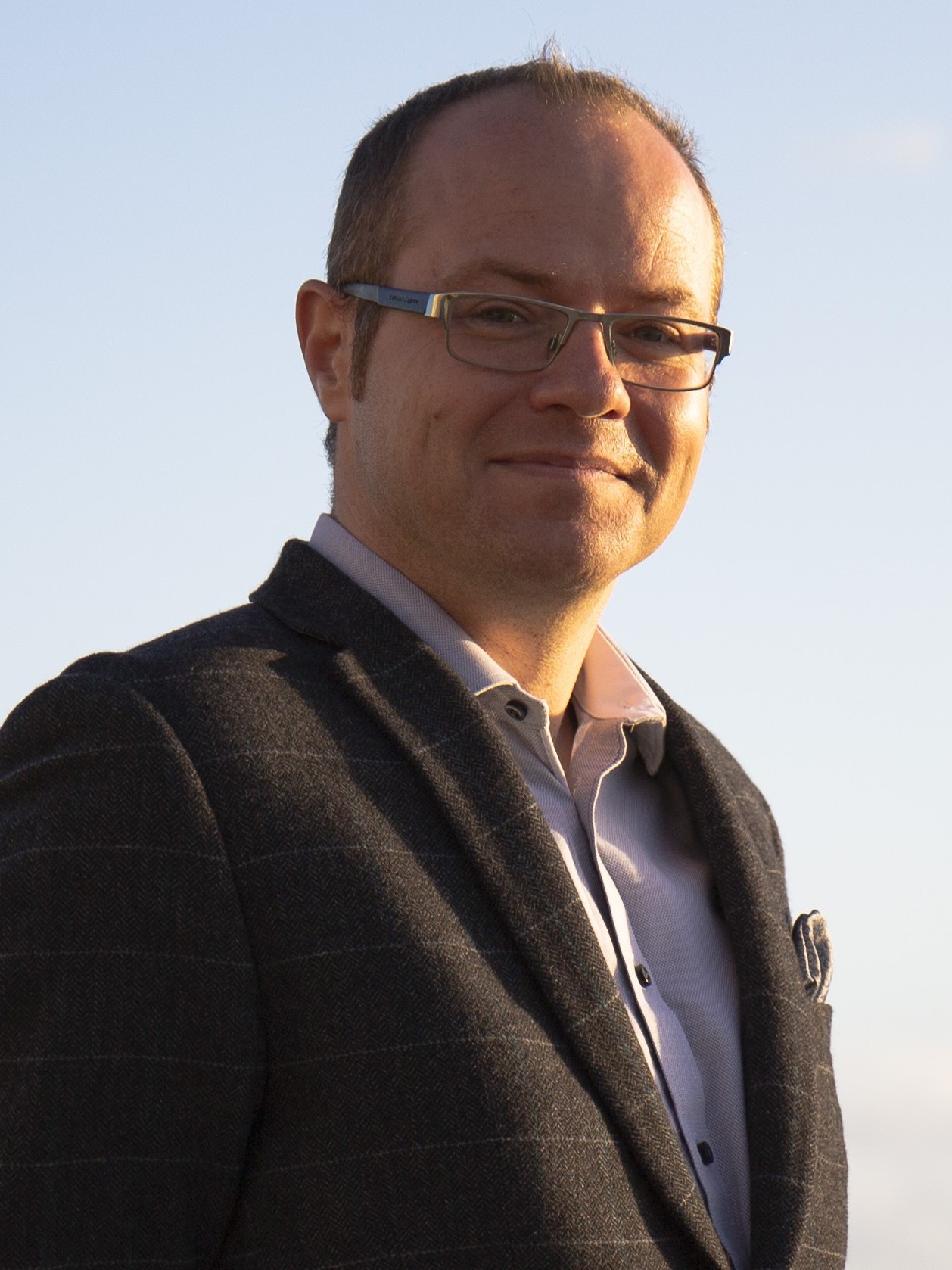 Portrait of Benjamin Sovacool, smiling at the camera in a dark grey blazer and glasses