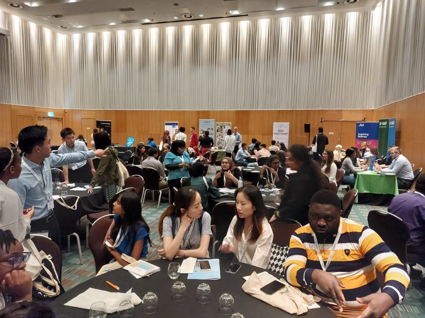 Students mingle at tables at stalls in a large conference room Students mingle at tables at stalls in a large conference room
