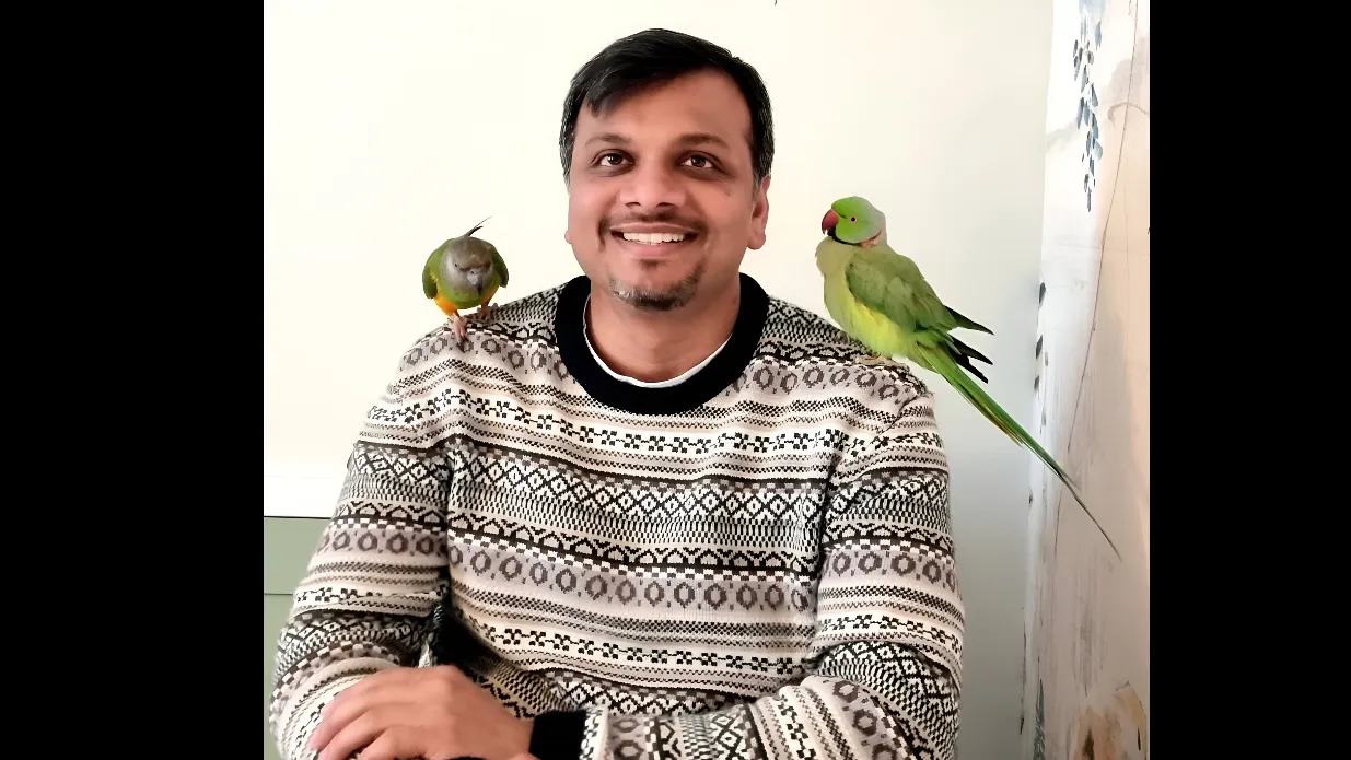 Dr Amit Kumar smiling for camera with two parakeet birds on his shoulder