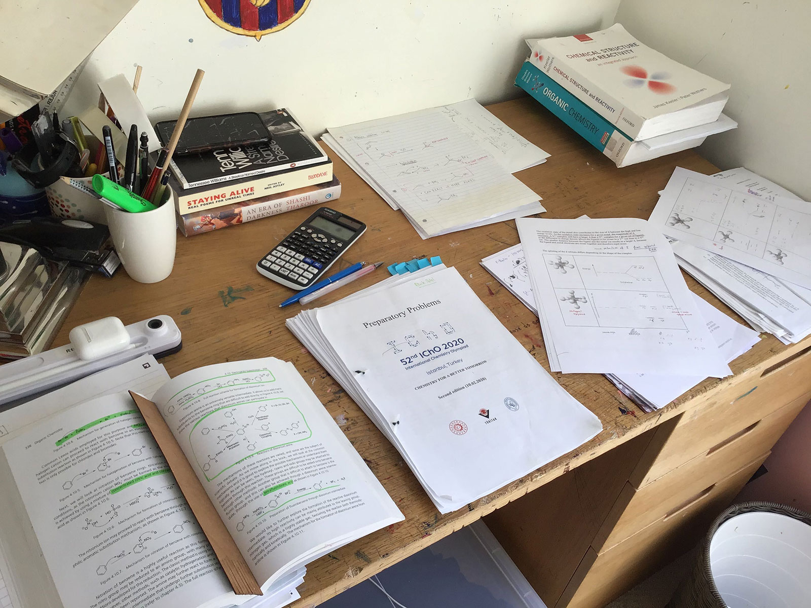 A desk with writing materials and sheets of paper containing chemistry questions. A desk with writing materials and sheets of paper containing chemistry questions.