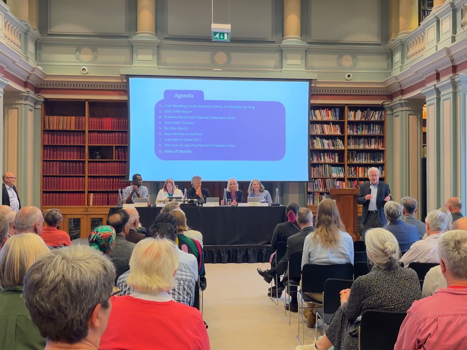 The library at Burlington House, filled with people seated in an audience and a panel of speakers seated on a rostrum at the front of the room The library at Burlington House, filled with people seated in an audience and a panel of speakers seated on a rostrum at the front of the room