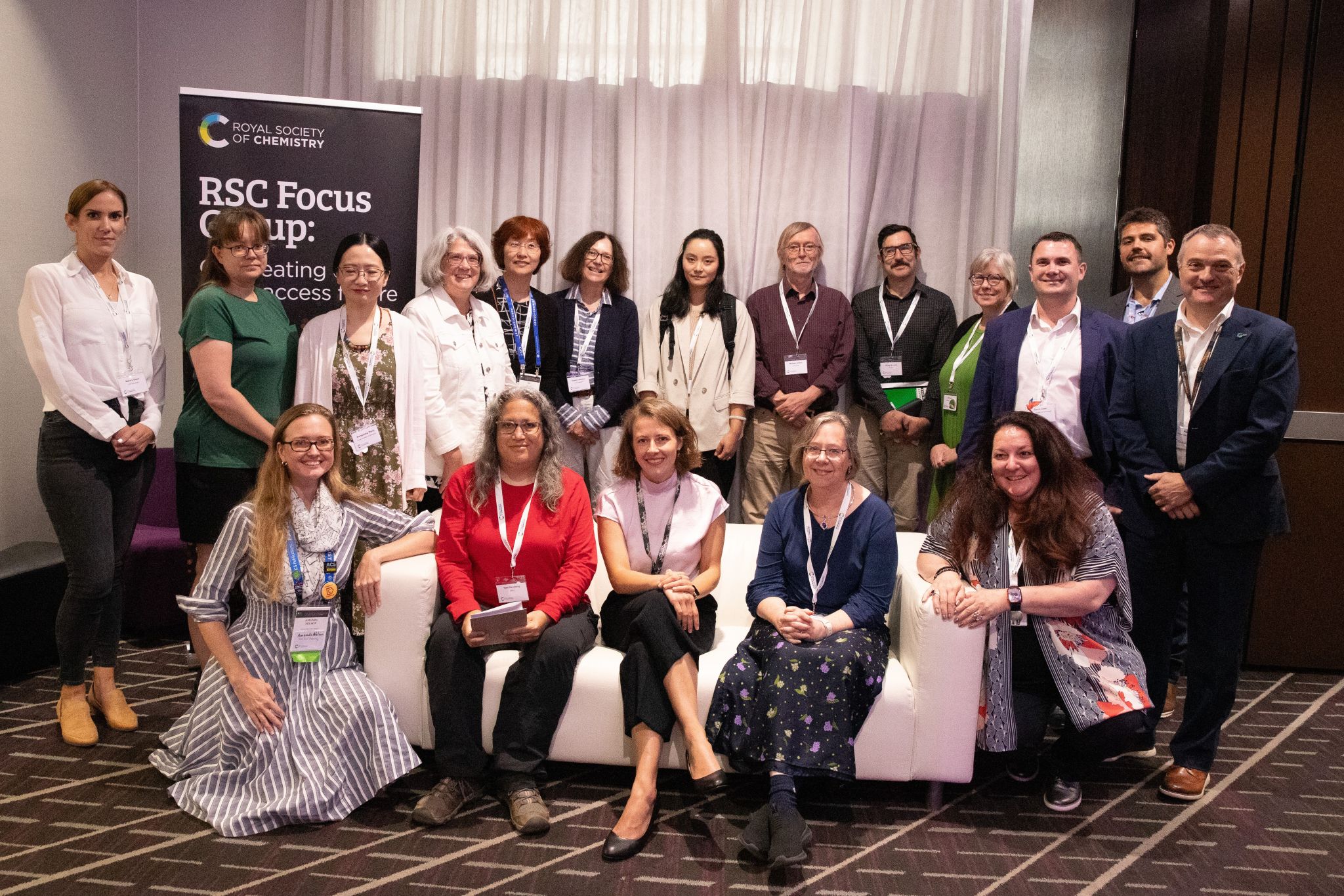 The Royal Society of Chemistry's Open Access transition focus group (13 people in the back row and five people down in front) poses together in front of an RSC banner in a conference room at an American Chemical Society Fall event. RSC Head of Open Access Sara Bosshart is sat in the middle of the front row.
