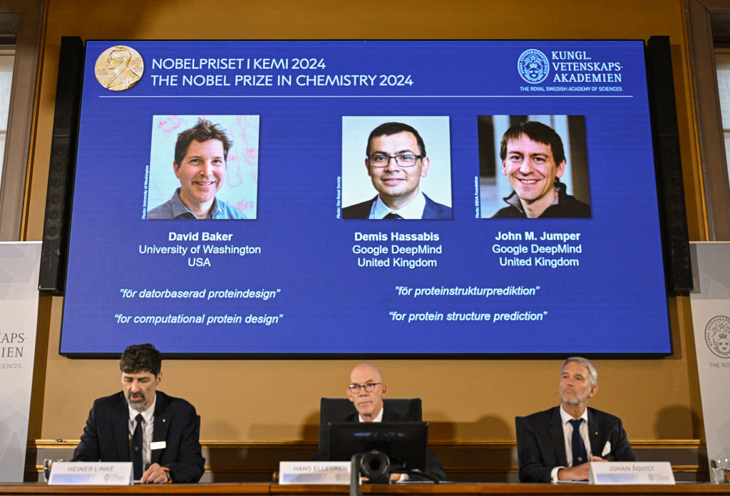 (Bottom L-R) Chair of the Nobel Prize Committee for Chemistry Heiner Linke, Secretary General of the Royal Swedish Academy of Sciences Hans Ellegren and Member of the Nobel Prize Committee for Chemistry Johan Aqvist announce the laureates of the 2024 Nobel Prize in Chemistry, (On screen L-R) David Baker, Demis Hassabis and John M Jumper, at the Royal Swedish Academy of Sciences in Stockholm, Sweden on October 9, 2024. The Royal Swedish Academy of Sciences has decided to award the 2024 NobelPrize in Chemistry with one half to David Baker "for computational protein design" and the other half jointly to Demis Hassabis and John M. Jumper "for protein structure prediction."