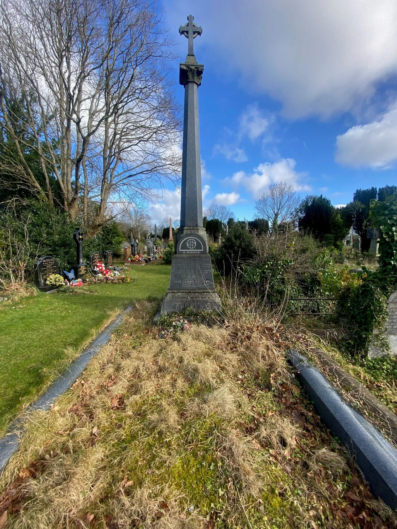The grave was in an overgrown state before the restoration, with long grass and weeds surrounding the unkempt base
