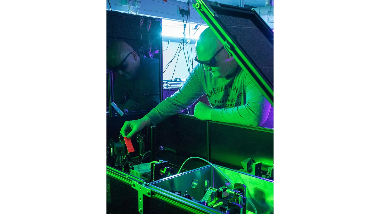 Dr Jack Woolley working on a machine in green light and wearing black safety goggles